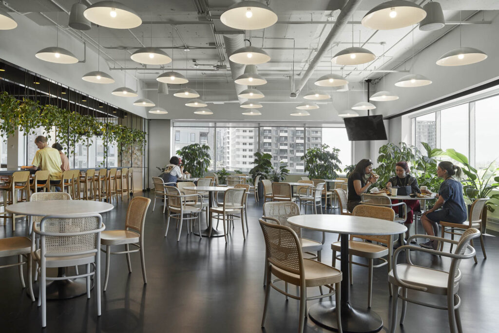 rows of pendant lights hang from the ceiling and plants adorn the space in the café of an office