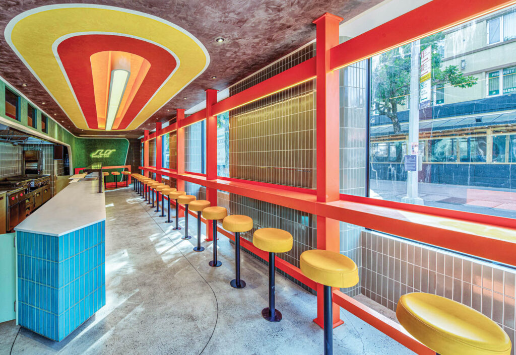 Vibrant hues of orange, red and yellow enliven this burger bar with a bright blue countertop and yellow stools reminiscent of a 70s retro diner