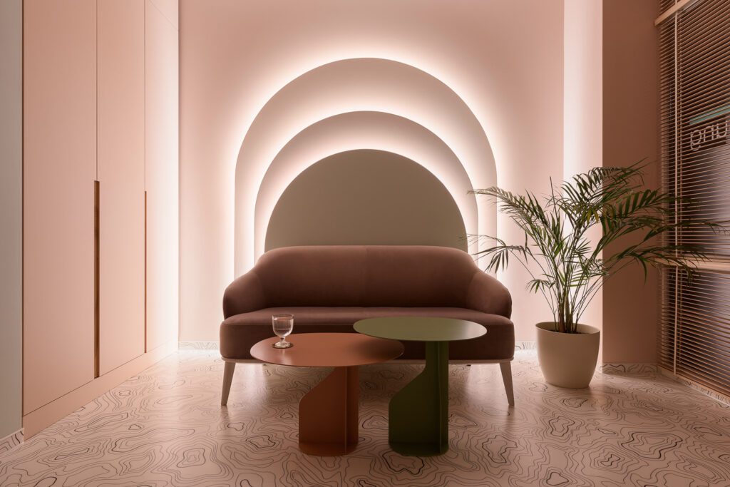 A maroon sofa sits in front of a backlit pale pink wall in a women's medical facility.
