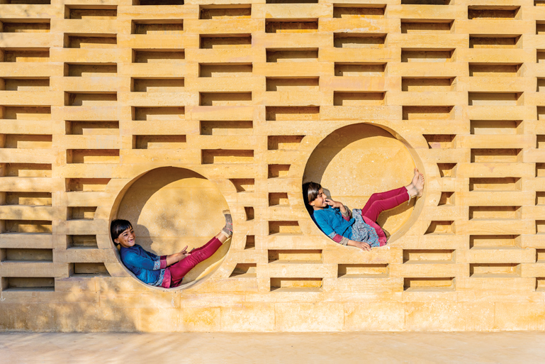 Two children sit in circles of hand-carved sandstone in the building facade