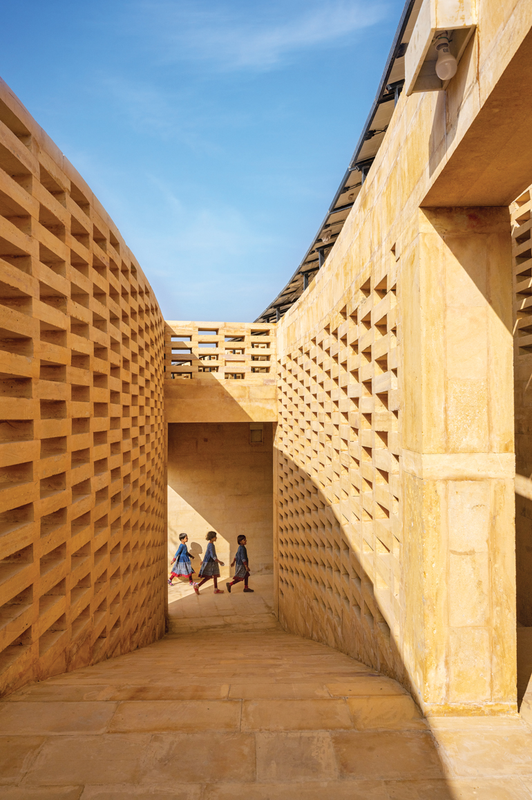 Three girls walk down a hall between lattice sandstone work that opens to the sky