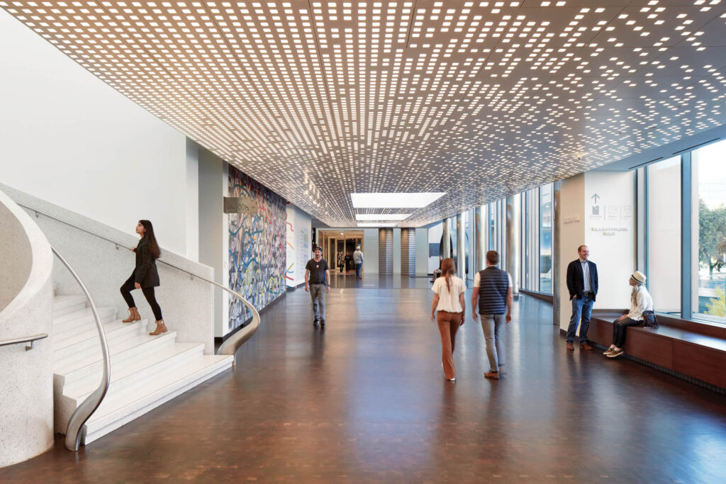 people walk throughout a hallway inside the Denver Art Museum, with a ceiling made of cutout small squares
