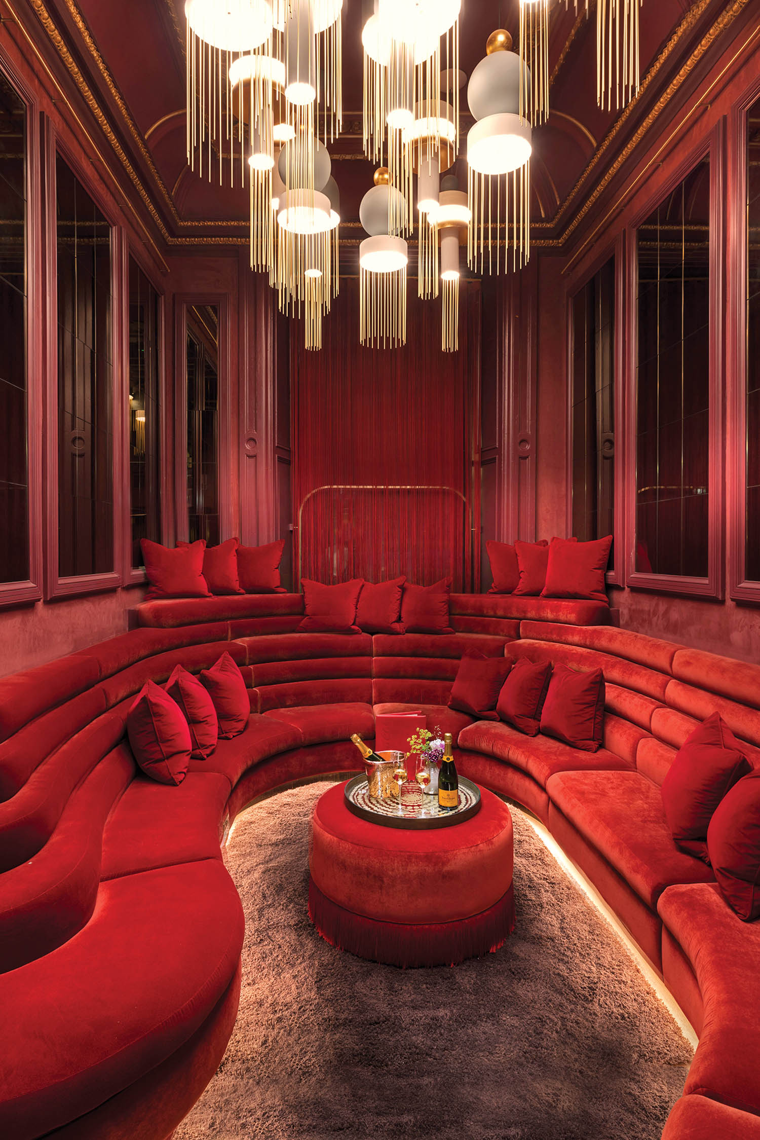 a red curving sofa under chandeliers in a room at the Virgin Hotels Edinburgh