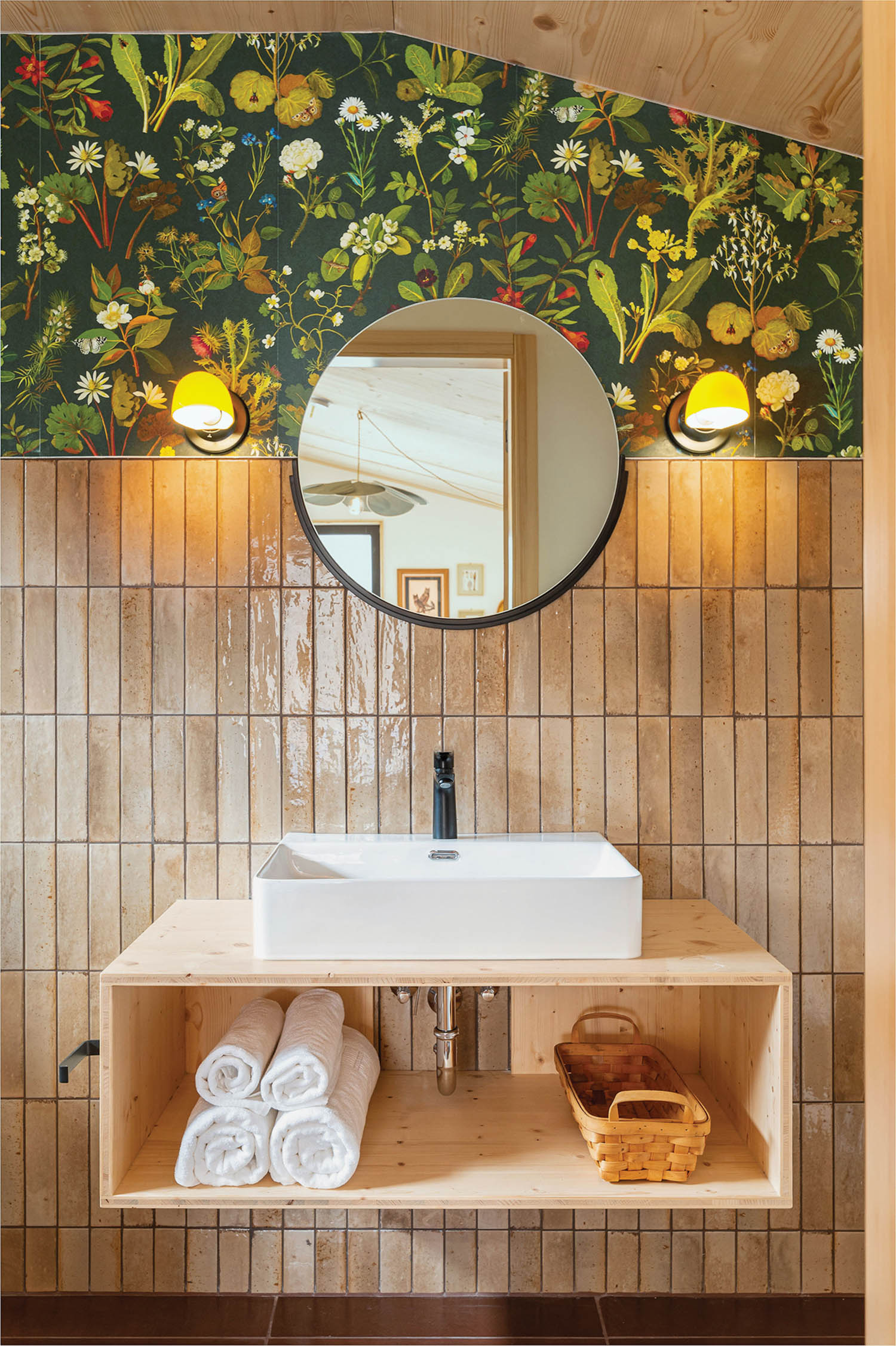 a bathroom in a rustic cabin with tan vertical tiles topped with green floral wallpaper