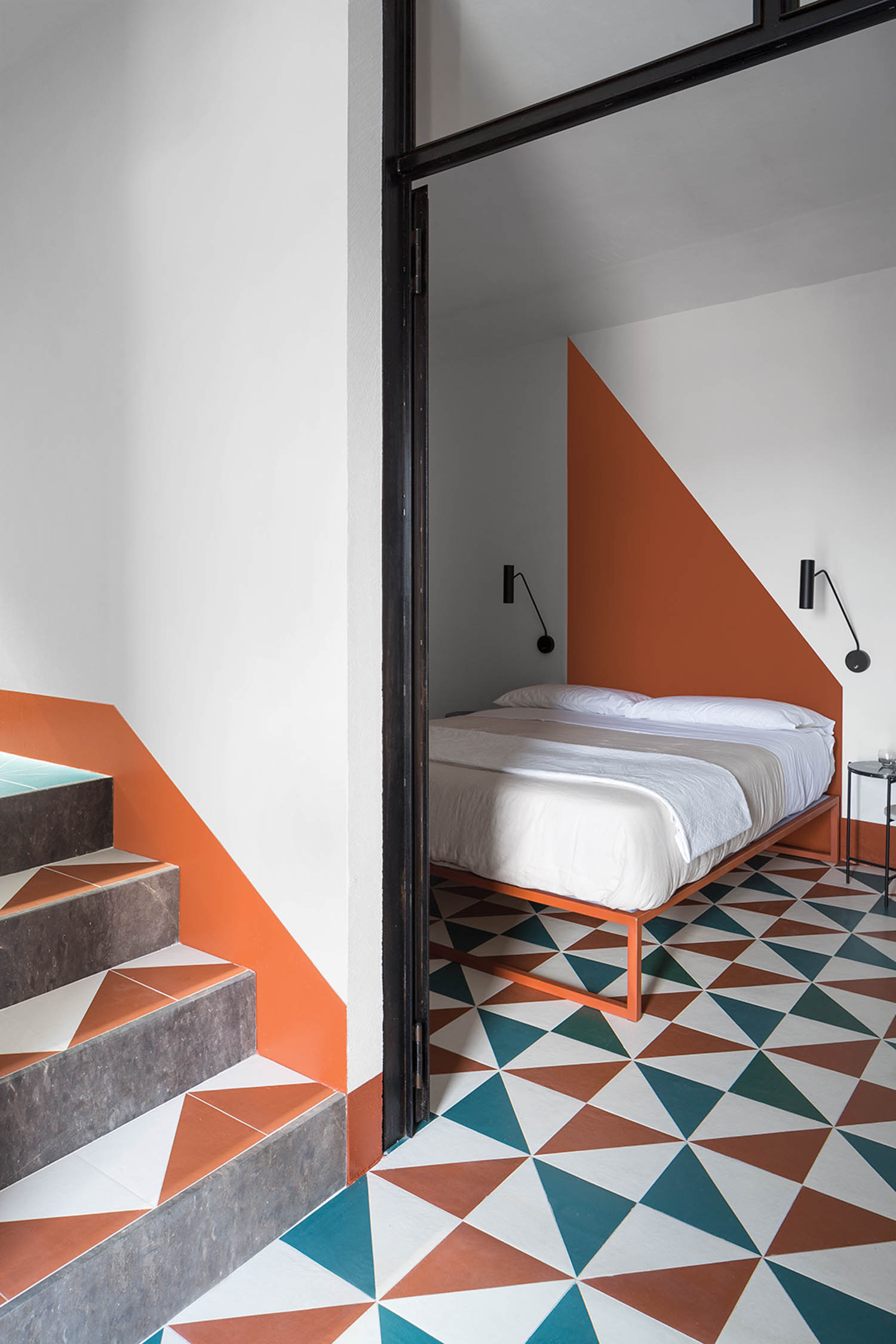 a bed lies atop a teal and orange tile with a matching painted orange triangle forming a headboard