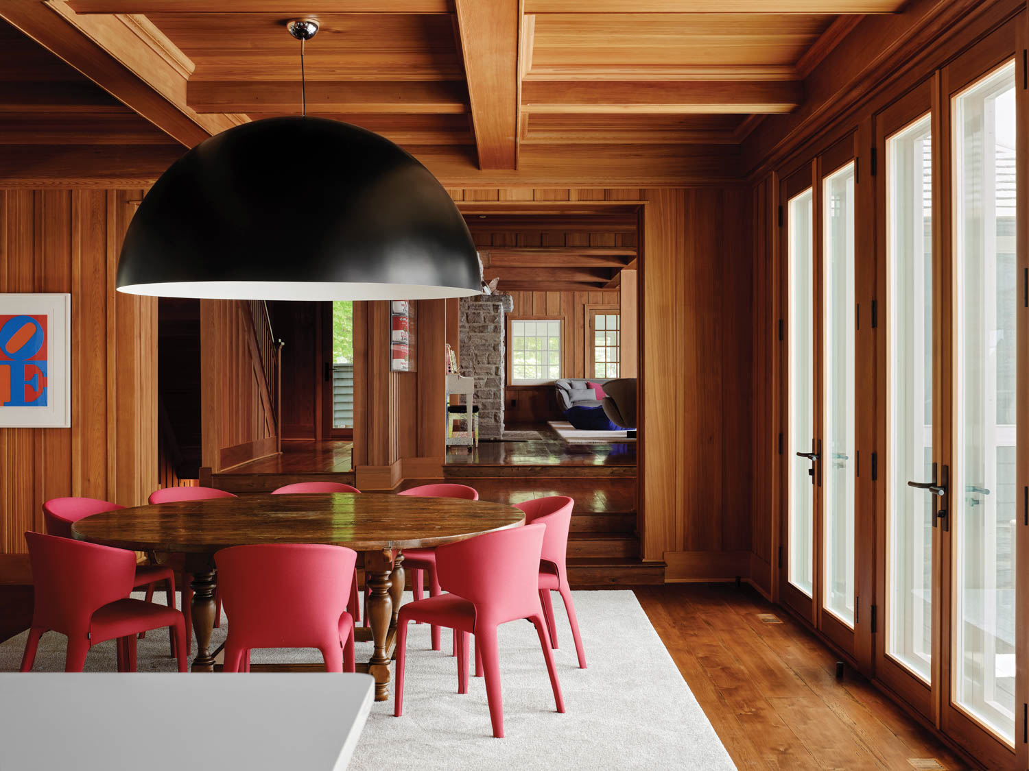 red chairs surround a dining table under a large black pendant light in a cottage