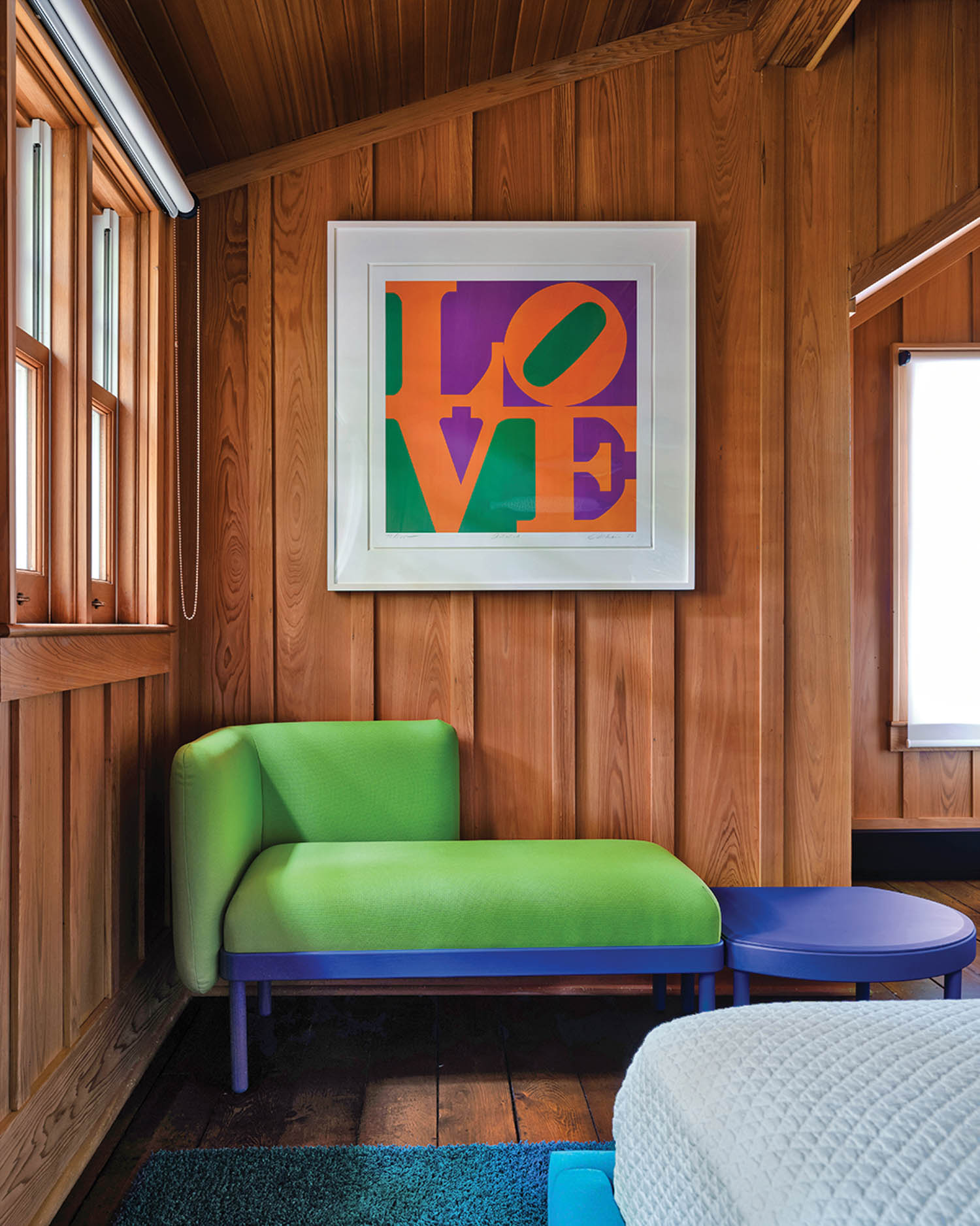 A Robert Indiana "Love" print on the wall above a green sculptural seat