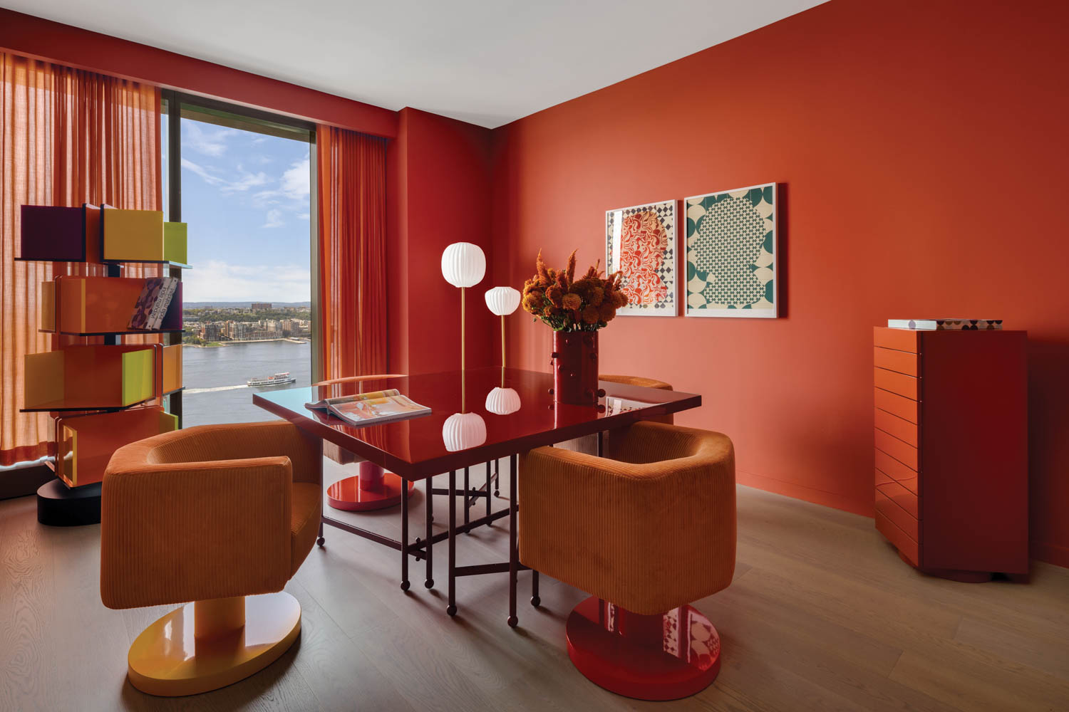 A home office with orange walls and orange chairs around a glass table