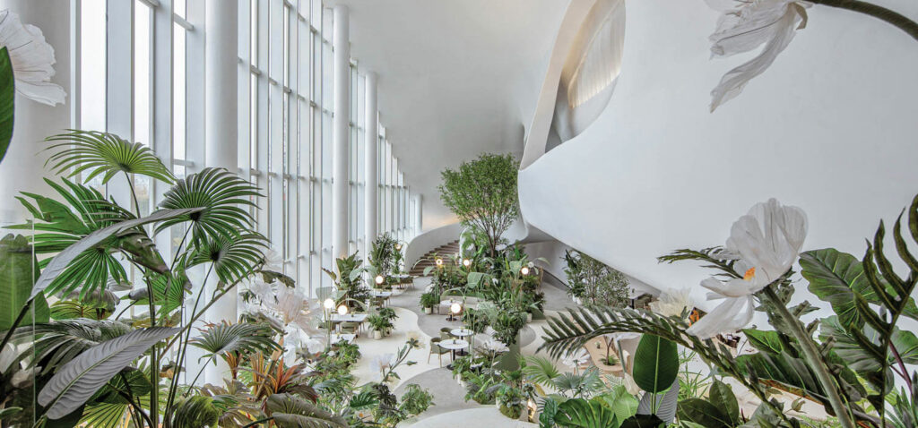 a white room with floor to ceiling windows and lush greenery throughout