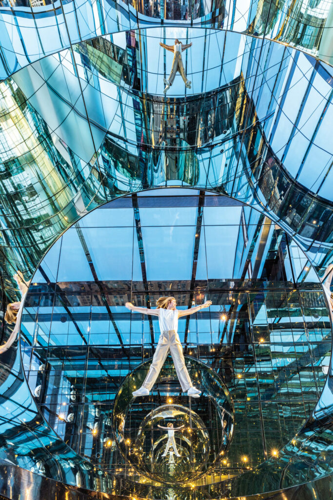 a person lies on the ground of Summit One Vanderbilt, with their reflection duplicated throughout the mirrored space