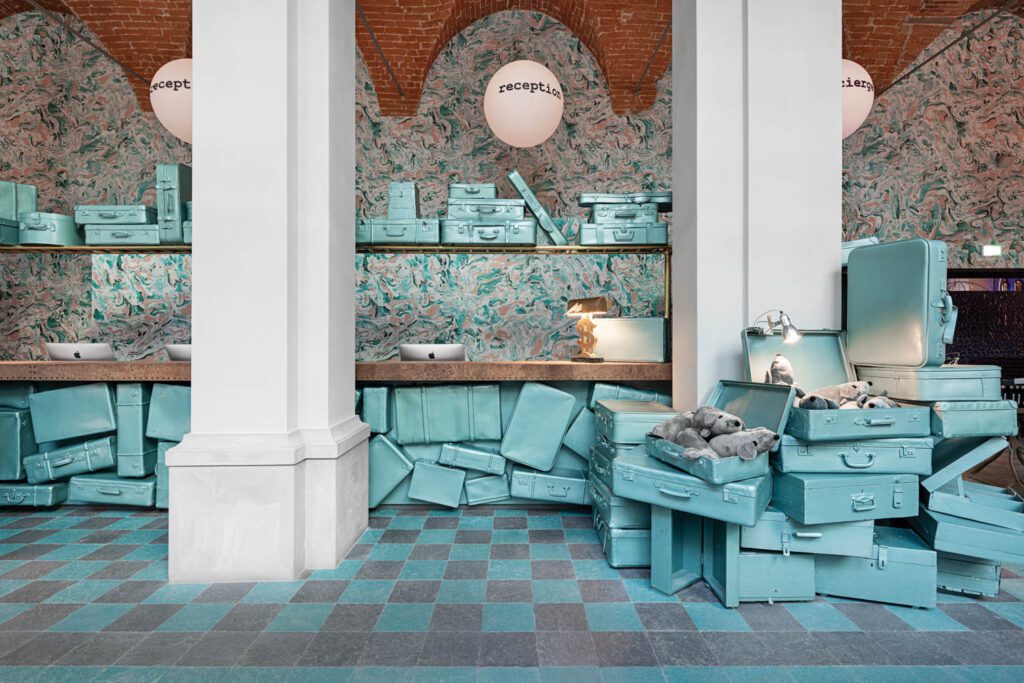 Piles of old, painted suitcases form a reception installation at 25hours Hotel Piazza San Paolino in Florence, Italy, an interiors project by Paola Navone’s Otto Studio that was inspired by Dante Alighieri’s 14th-century poem, The Divine Comedy.