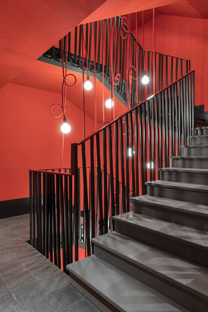 A stairwell’s wall color and pendant fixtures suggest a descent into hell.