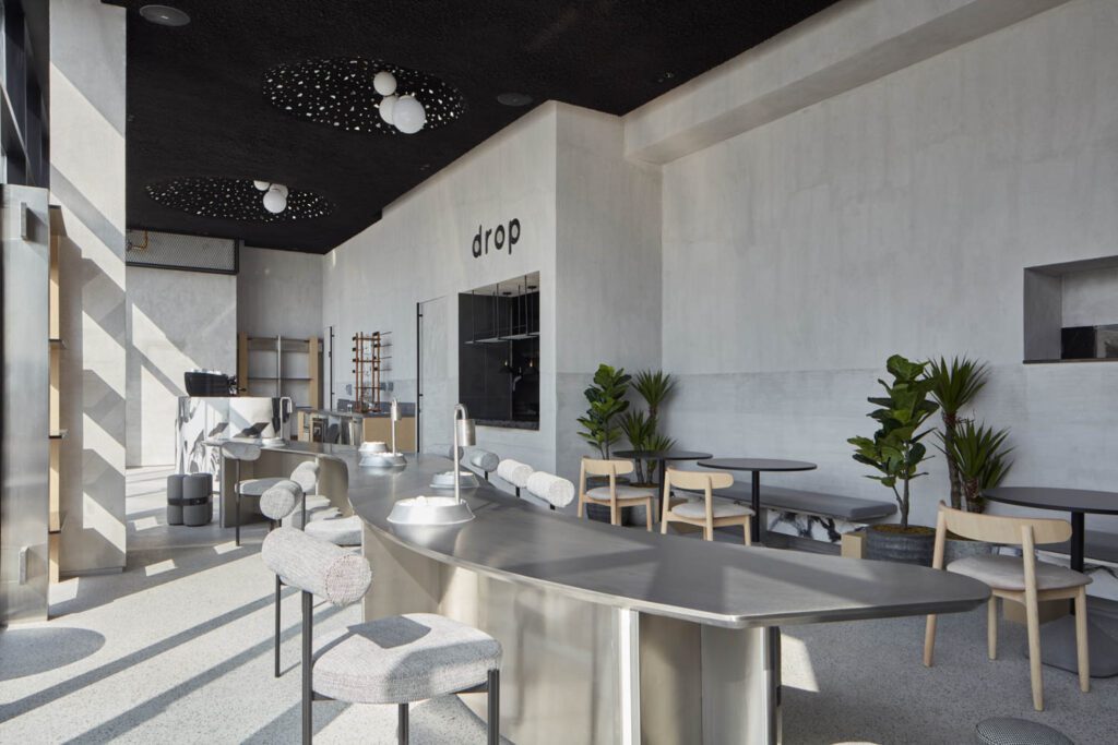 Concrete-effect textured paint coats all walls in Drop Abu Dhabi, the Emirati coffee chain’s new outpost designed by Dubai-based studio Roar.