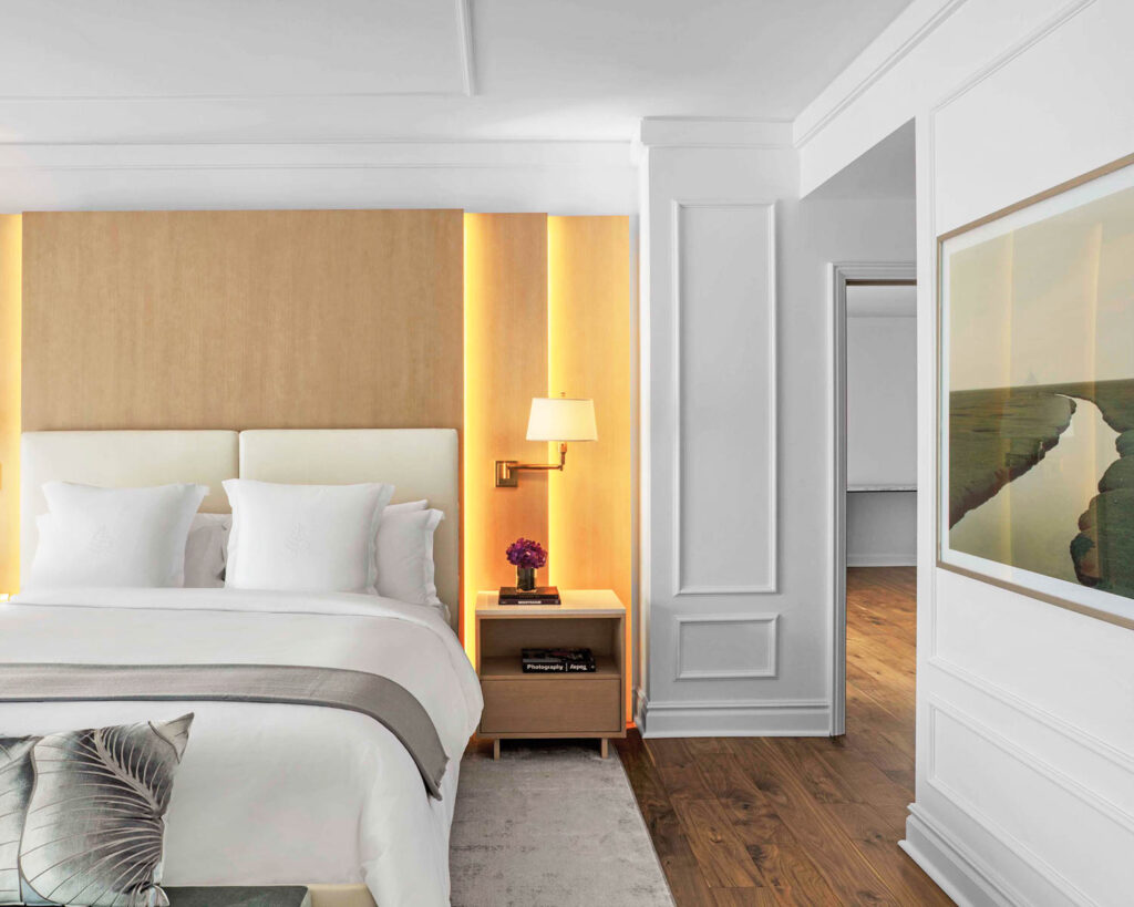 a guest suite in the Four Seasons featuring a plush bed and lit wall sconce lamp