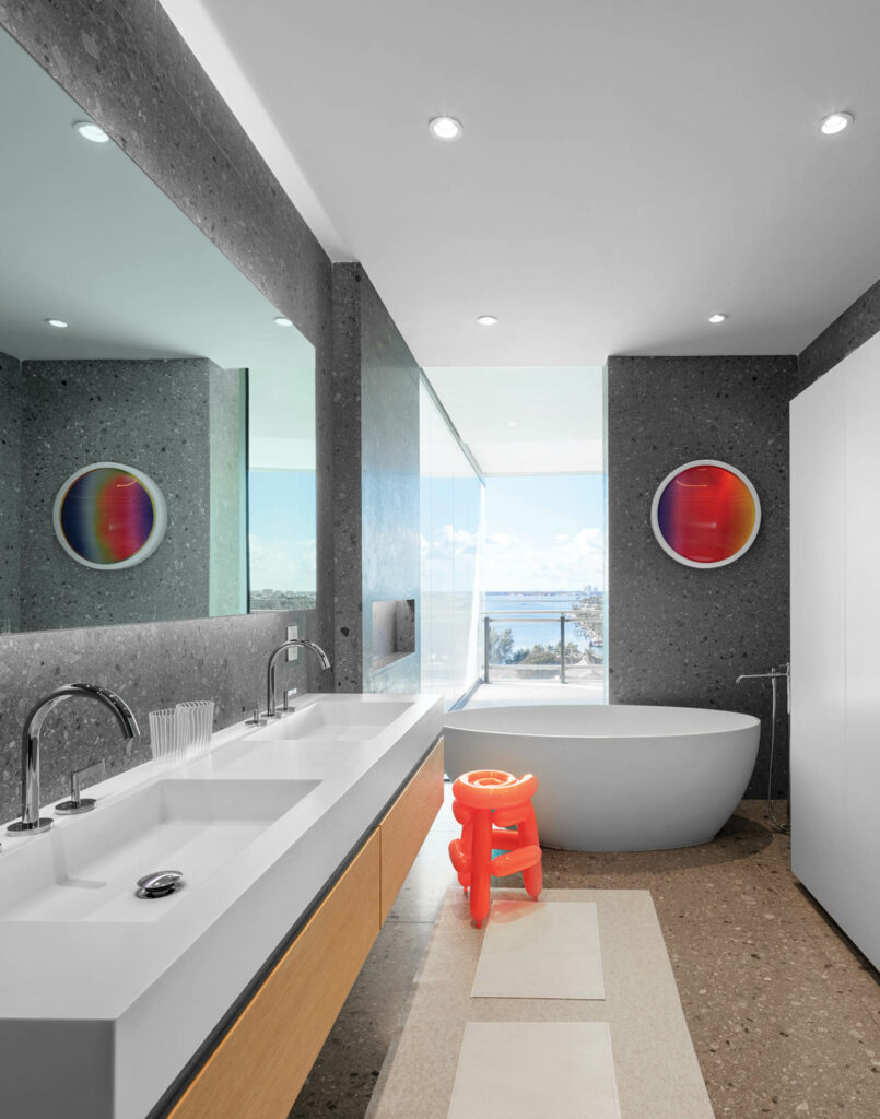 a colorful round artwork hangs above the tub with a neon orange stool beside it in this bathroom