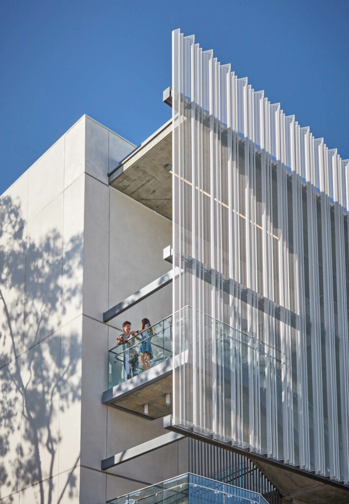 students stand on a balcony behind a screen on the exterior of an undergrad building at Loyola Marymount University