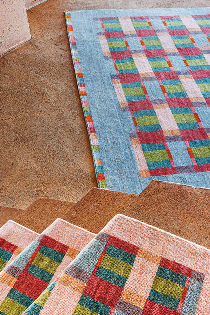a pink rug with red and green geometric shapes lies next to a blue rug of the same pattern