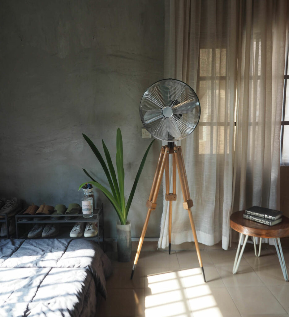 A wooden tripod base for a fan in a room with a stool and curtained window