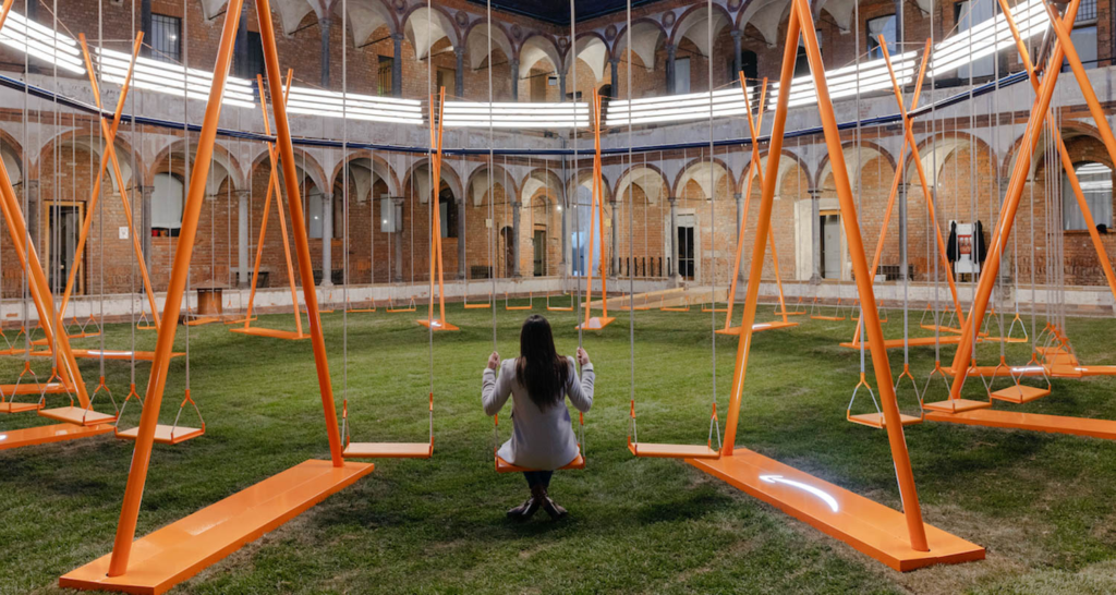 a girl sits on a swing on an oversized swing set at the University of Milan